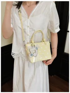 Gelbe Polka-Dot-Eimertasche mit Notenanhänger, getragen von Model im weißen Spitzenkleid