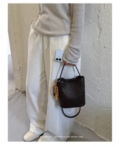 Lifestyle detail of a dark brown woven bucket bag held by a person in minimalist clothing