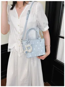 Hellblaue Handtasche mit Polka Dots, Noten-Anhänger und Spitze an Modell präsentiert.
