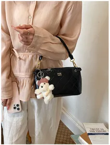 Detailed shot of a black quilted leather shoulder bag with a bear charm and gold hardware