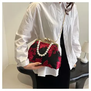 Detail view of elegant black evening bag featuring red 3D floral embroidery and pearl handle