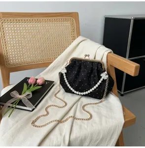 Detalle de bolso de noche negro bordado con flores y correa de perlas en una silla