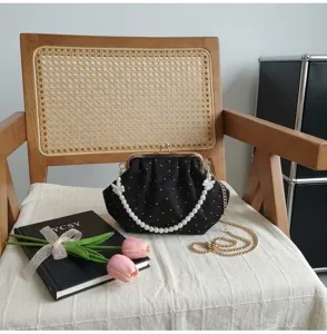 Elegante bolso de noche negro con correa de perlas y cadena en una silla de madera