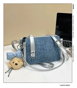 Close-up of denim shoulder bag with silver hardware and cute bear charm.