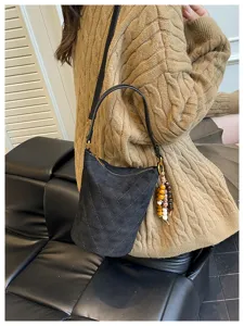 Primer plano de un bolso bucket acolchado negro con adorno de madera usado por una modelo