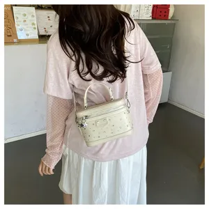 Detail view of a stylish cream rhinestone vanity box bag worn crossbody by a model.
