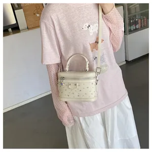 Close-up of an elegant off-white box handbag with silver studs worn by a female model.