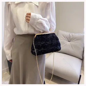 Black floral evening clutch bag with gold chain and rhinestone clasp held by a model.