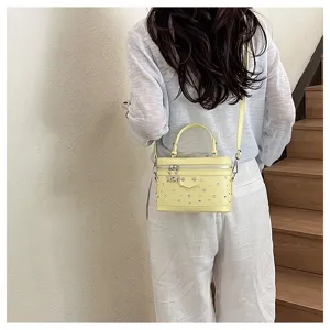 Pale yellow studded vanity box bag shown on shoulder in a lifestyle setting