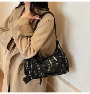 Chic black glossy motorcycle shoulder bag with buckle details shown on model.
