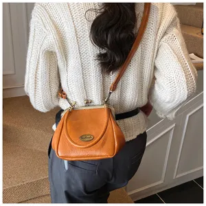 Vue de dos d'une femme portant un sac bandoulière rétro en cuir orange avec fermoir clic.