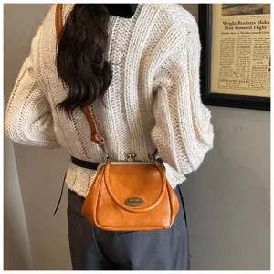 Sac à main vintage en cuir souple orange porté sur un pull en maille blanc douillet