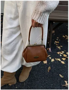 Vue détaillée d'un sac à main vintage marron avec fermoir à baiser en décor d'automne.