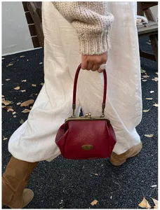 Vue détaillée d'un sac à main bordeaux vintage à fermoir à baiser tenu par un mannequin