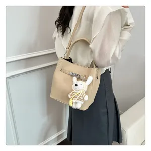 Detailansicht einer beigen Eimertasche mit Lychee-Muster, klassischem Schloss und süßem Hasenanhänger