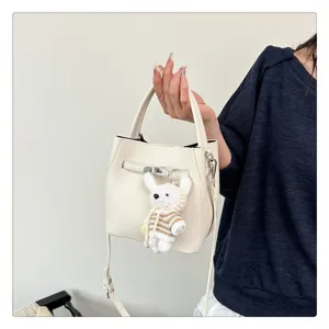 Elegante cremeweiße Eimertasche mit Lychee-Muster, Metallschloss und süßem Bärenanhänger