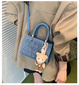 Detail of denim blue woven mini tote bag with sequins and bear charm worn by a person