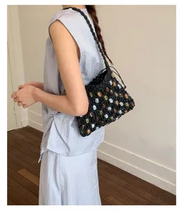 Detailed view of a black woven beaded drawstring bucket bag worn on the shoulder.