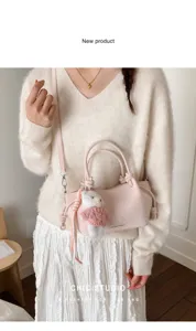 Nahaufnahme der rosa gefalteten Beuteltasche mit Bärenanhänger auf weißem Pullover