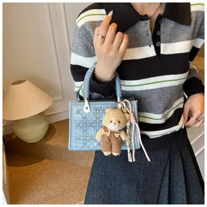 Detailed view of a light blue denim tote bag featuring woven handles and bear charm.