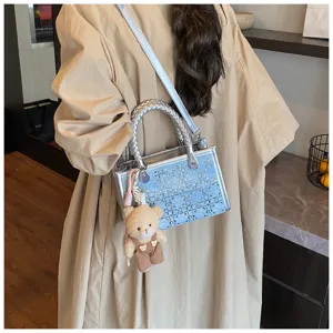 Detail view of a light blue denim tote bag with silver handles and a cute bear charm.