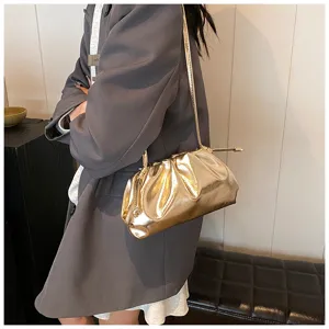 Stijlvol mode-model draagt een gouden geplooide wolkentas met een grijze blazer aan.