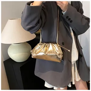Detailopname van een goudkleurige geplooide wolkentas gedragen met een grijze blazer.