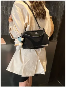 Back view of model wearing a black soft fabric shoulder bag with teddy bear charm