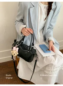 Sac Boston en cuir noir avec breloque ours, porté avec un blazer et une robe blanche