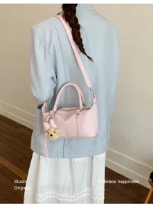 Modèle portant un élégant sac polochon en cuir rose avec breloque ours en peluche