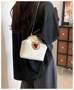 Detail van witte geborduurde schelptas met rood hart en een gouden ketting