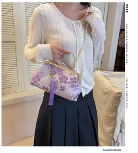Elegante Abendtasche mit Blumenstickerei, lila Quaste und Perlenriemen in der Hand.