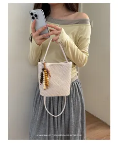 Close-up of a woven texture bucket bag with bead charm held by a model in a retro style