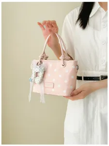 Rosa gepunktete Handtasche mit Noten-Anhänger, gehalten von Model in Weiß