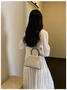Close-up of floral embroidered bag with bamboo handle worn over a white dress