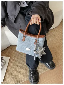 Détail d'un sac seau en denim avec des poignées marron et un pendentif étoile argenté