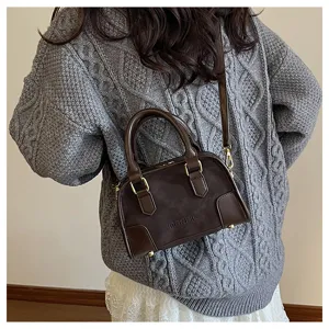 Close-up detail shot of a soft brown leather pillow bag worn crossbody over a grey sweater