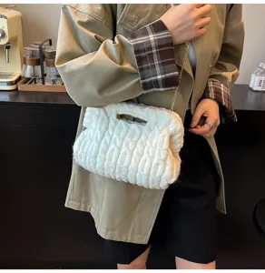 Detailopname van een witte gebreide tas met gouden ketting gedragen bij een beige jas