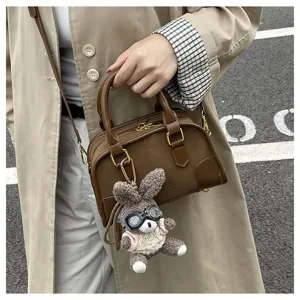 Close-up of minimalist brown leather pillow bag with cute bunny plush pendant.