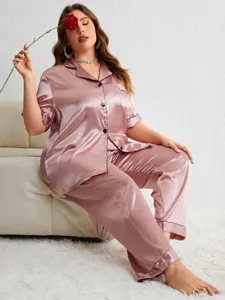 Model wearing plus size pink satin pajama set sitting on a white sofa in a home setting
