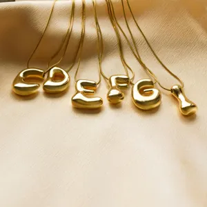 Detail of gold-plated balloon bubble alphabet pendant necklaces on silk fabric.