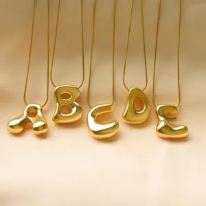 Detailed view of gold plated bubble letter pendants A to E on silky champagne fabric backdrop