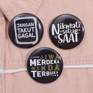 Close-up of black circular tinplate badges with inspirational text on pink fabric