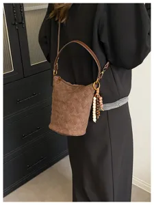 Vista detallada de un bolso de cubo acolchado marrón con borla de cuentas llevado por modelo