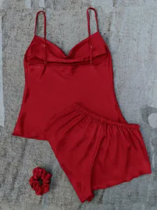 Detailed macro view of a red satin pajama set including camisole top, shorts, and scrunchie