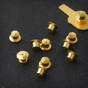 Close-up of golden metal pin backs for brooches and enamel pins on black surface