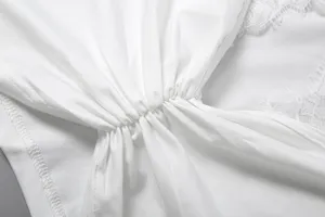 Close-up view of elegant white women's sleeveless top with lace patchwork and gathers.