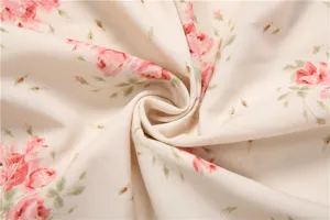 Close-up detail of soft beige fabric featuring elegant pink rose floral print and green leaves.