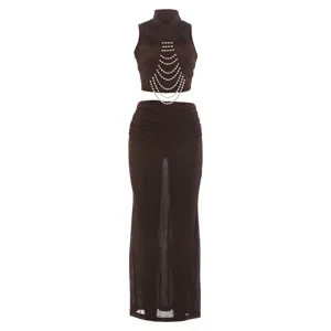 Close-up brown sleeveless mock neck crop top with layered pearl chain and sheer maxi skirt.