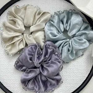 Detailed macro view showing three elegant satin scrunchies with luxury crystal beaded edges